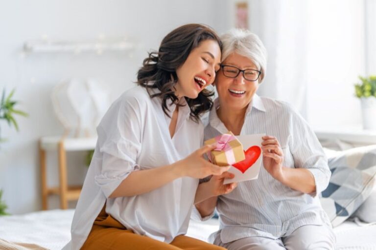 młoda kobieta wręcza starczej kobiecie prezent i kartkę z sercem