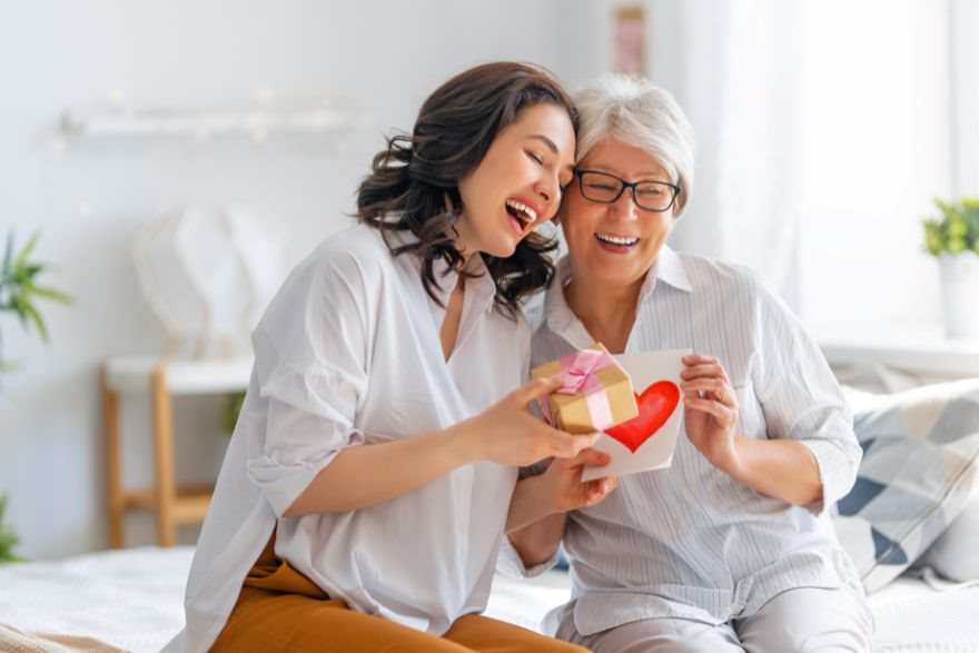 młoda kobieta wręcza starczej kobiecie prezent i kartkę z sercem