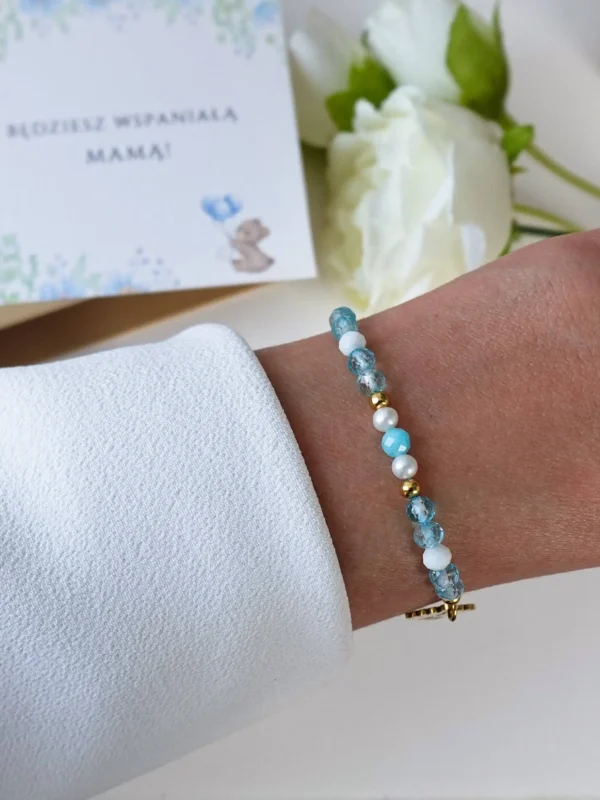 Bransoletka na Baby Shower dla przyszłej mamy spodziewającej się chłopca, z niebieskim topazem i zawieszką stópki, na nadgarstku.